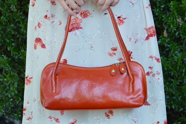 Orange Leather bag held by a person wearing a ivory and orange floral dress.