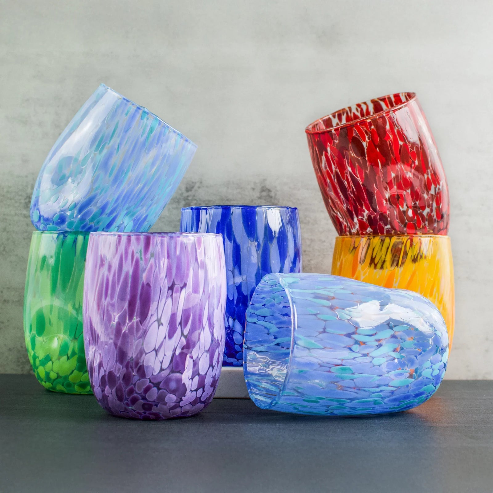 Colorful Murano Glass tumblers in red, blues, yellow, orange, red, green, and violet stacked up on a table.