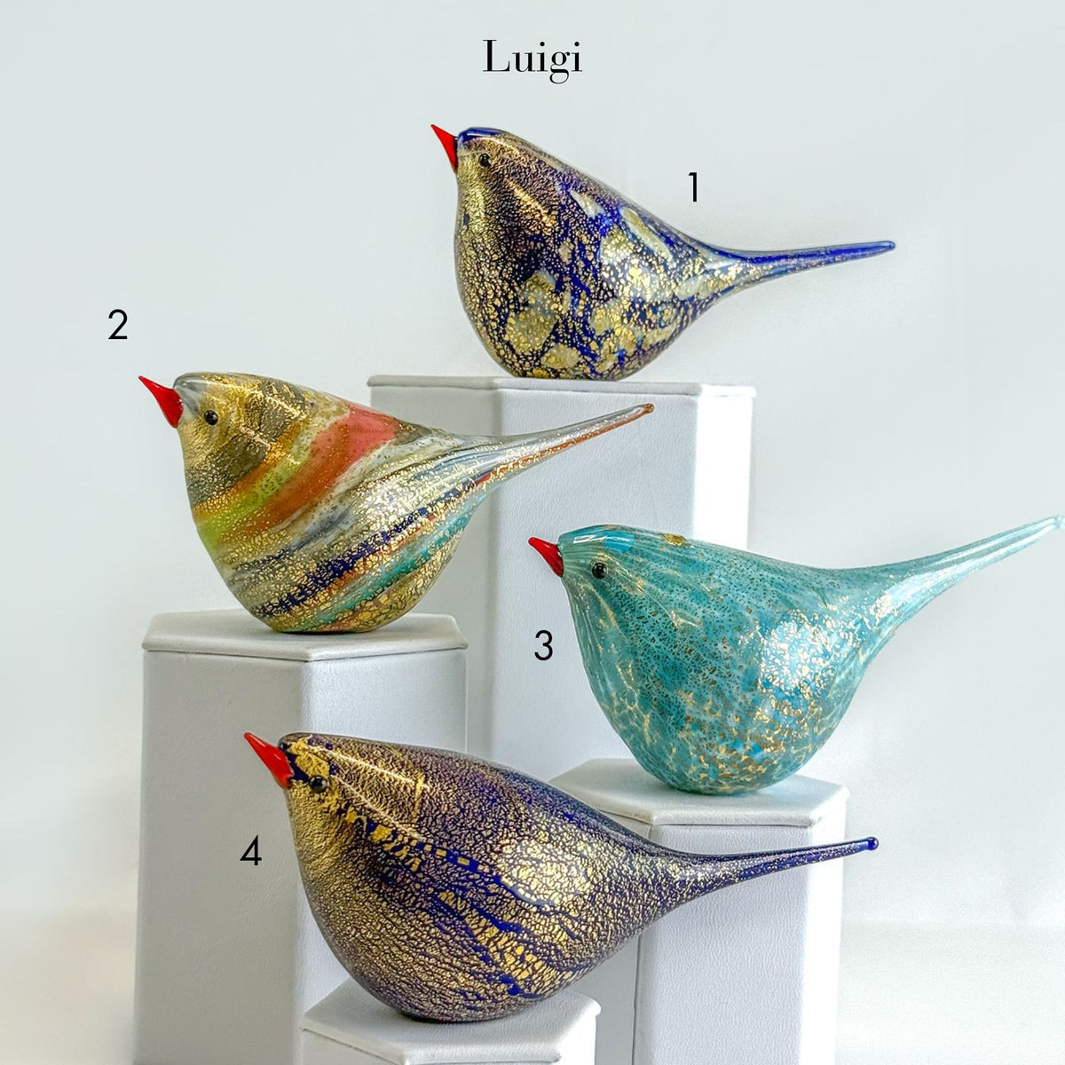 Four colorful glass bird sculptures on white pedestals with 'Luigi' branding.