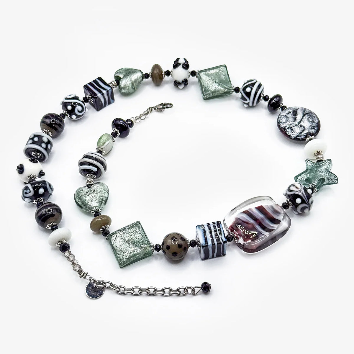 A handmade multi-strand beaded necklace featuring a mix of black and white patterned beads, translucent green glass beads, a large clear glass heart, and a striped glass cylinder, displayed on a clean white background.