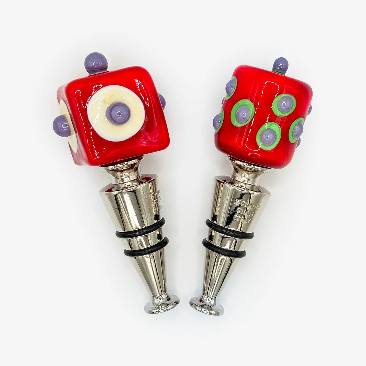 Two red glass wine bottle stoppers with silver metal bodies, one featuring a white circle with purple details and the other with green circles and purple dots, set against a plain white background.