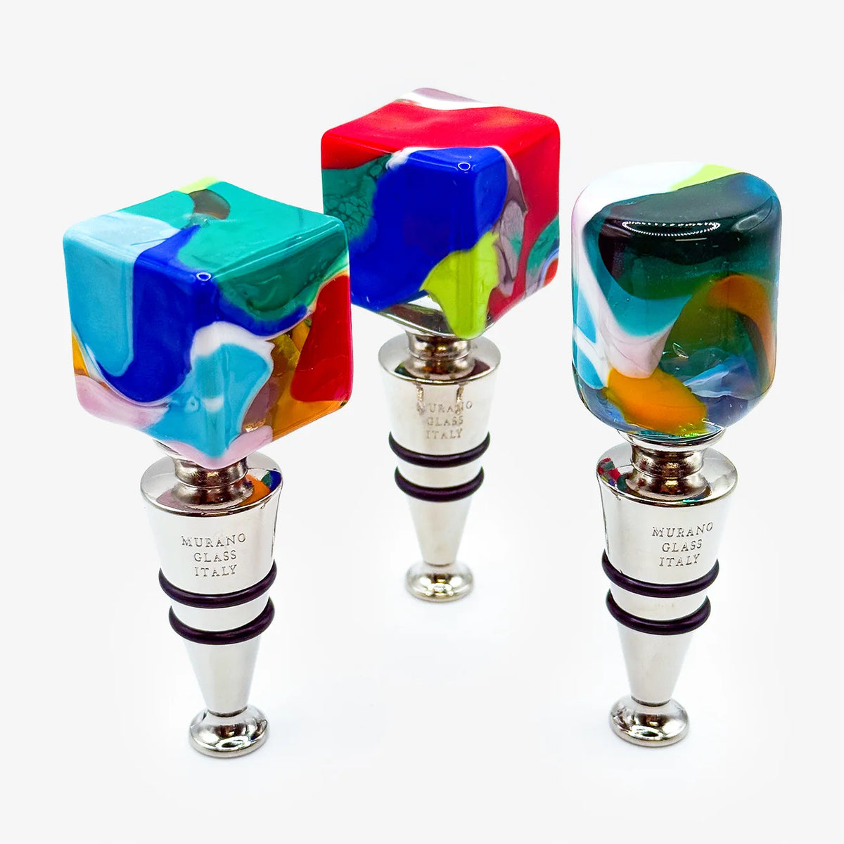 Three colorful Murano glass bottle stoppers with silver metal collars, displayed on a clean white background.