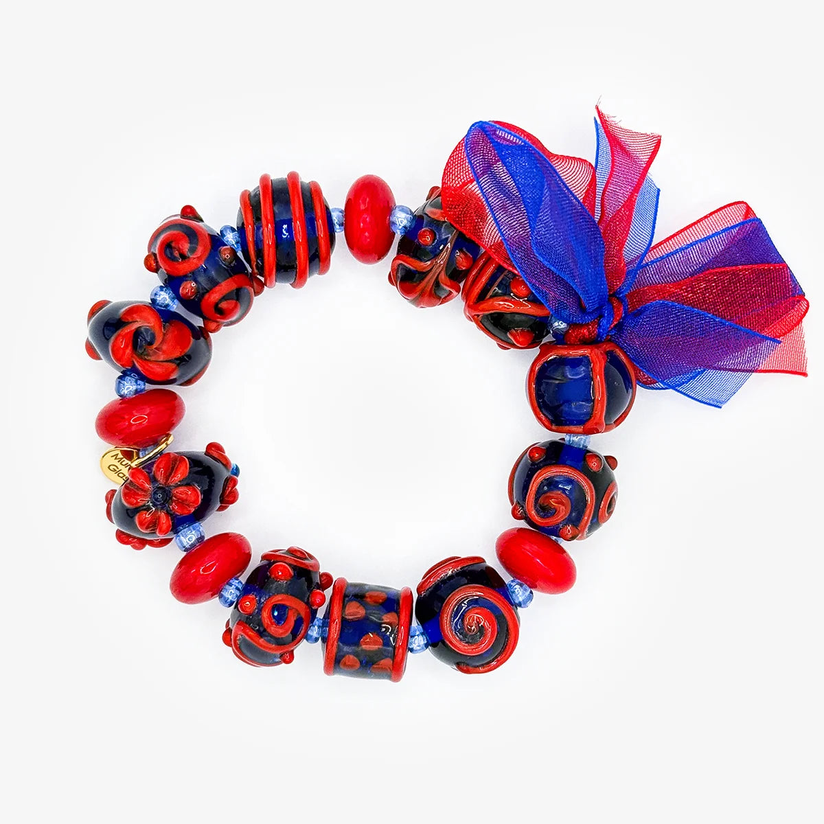 A jewelry set featuring a beaded bracelet and matching dangle earrings. The bracelet and earrings are decorated with red and black patterned beads, red and blue glass beads, a sheer red and blue ribbon bow, and colorful leaf and flower charms in green, blue, and red on gold-tone hooks.
