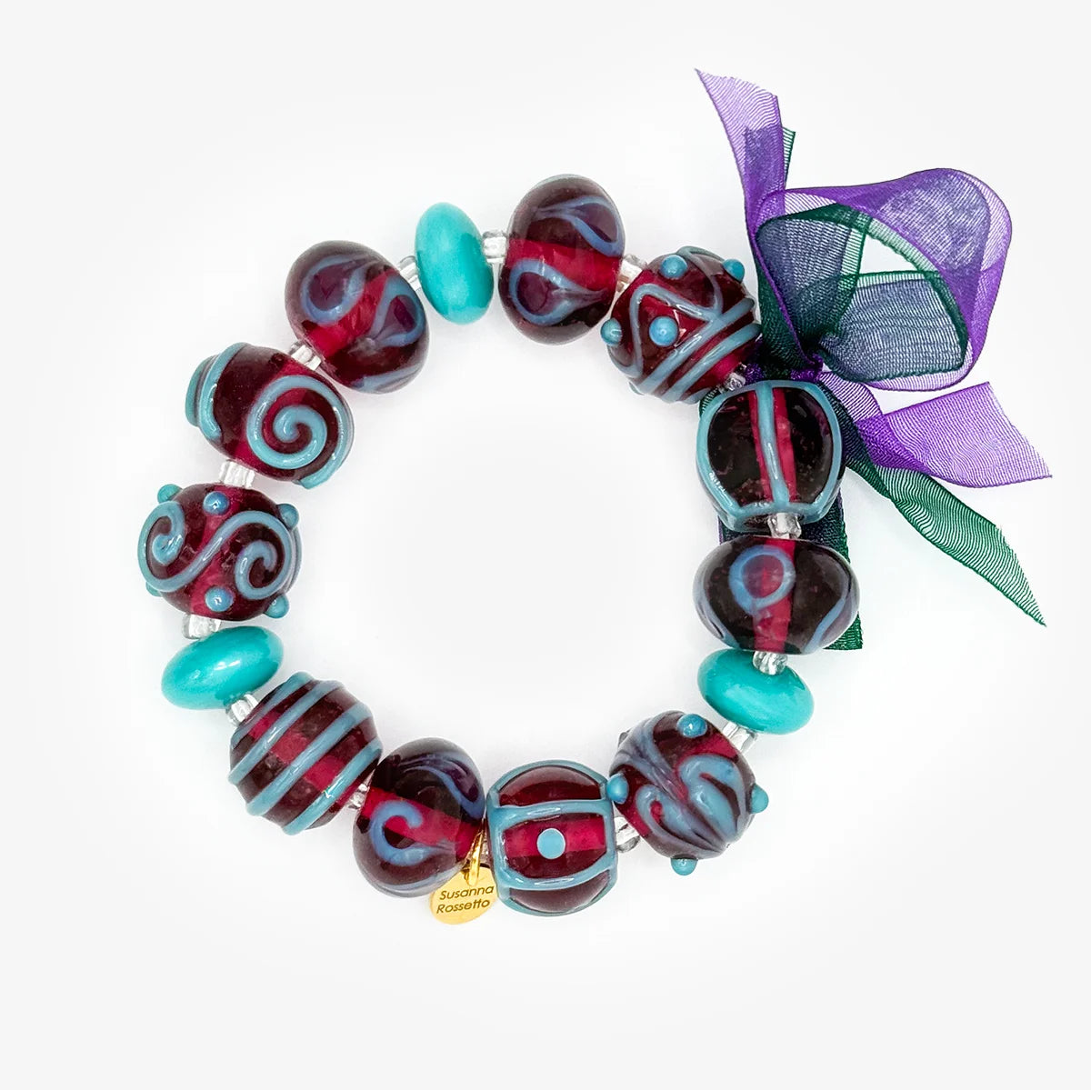A handmade jewelry set featuring a beaded bracelet and matching drop earrings on a white background. The beads are primarily deep burgundy with red swirls, turquoise blue accents, and a purple mesh ribbon bow.