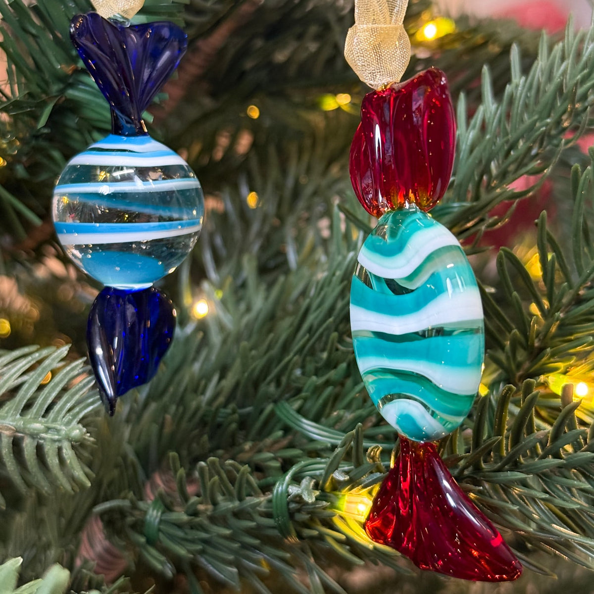 Decorative glass ornaments with blue, red, and green patterns hanging on a Christmas tree.
