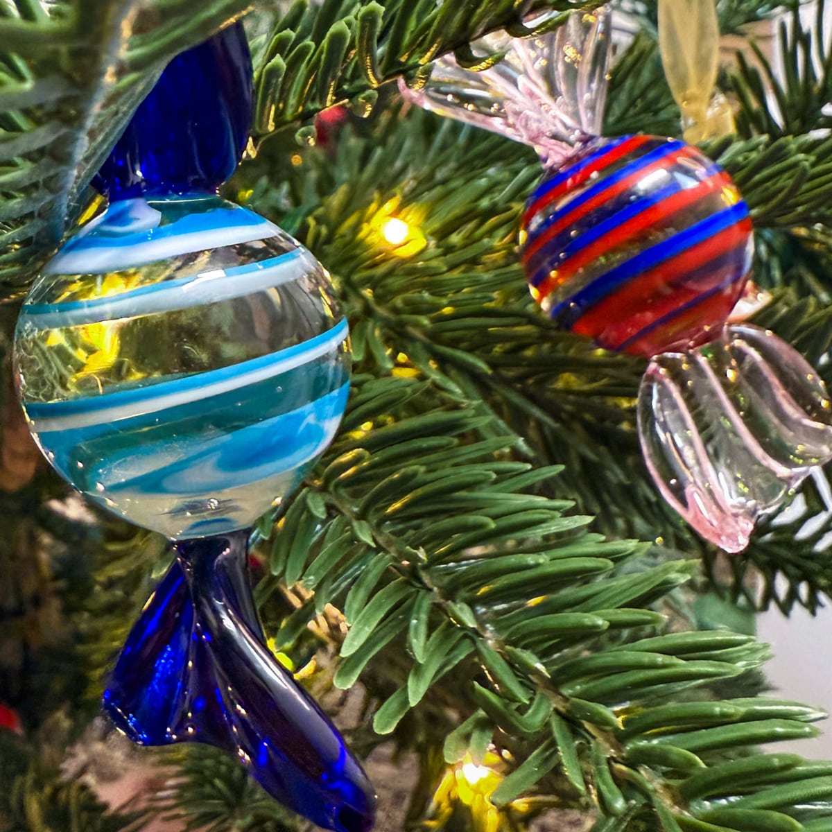 Decorative glass ornaments on a Christmas tree with blue, red, and clear colors.