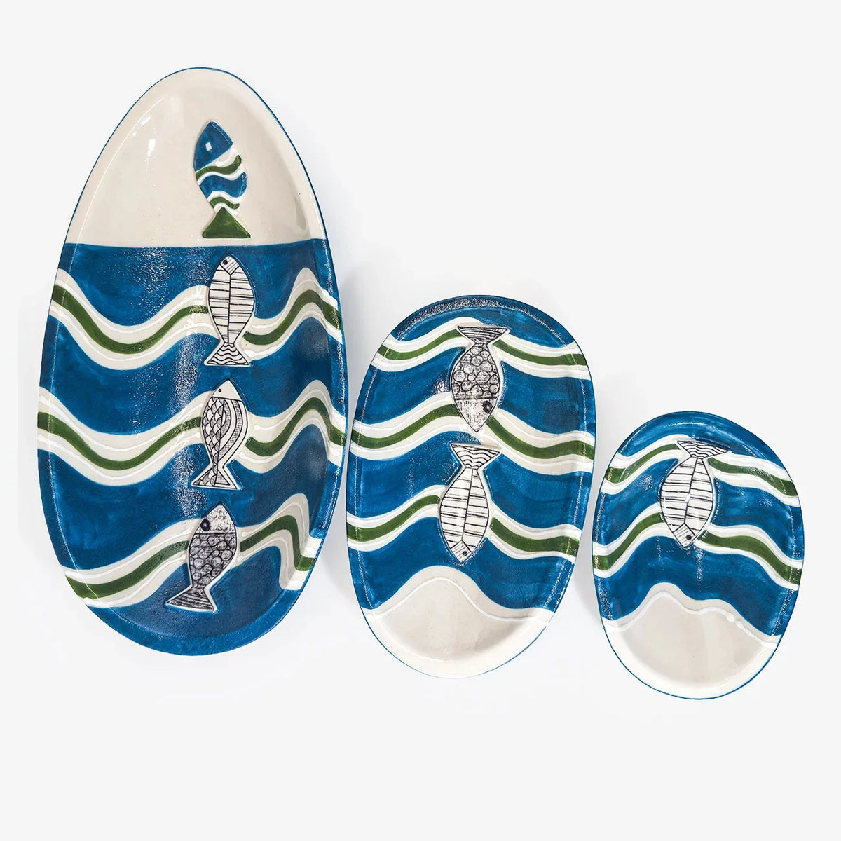 Three ceramic fish-patterned serving platters in different oval sizes, featuring blue and green wavy stripes and white fish motifs on a light background.