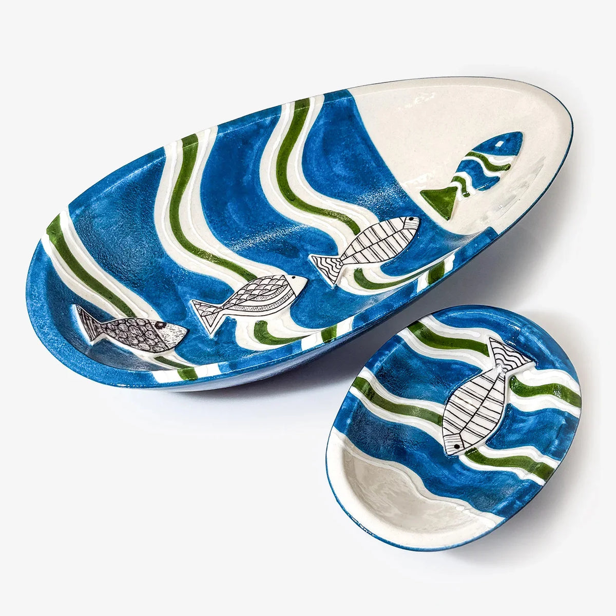 A ceramic serving set consisting of a large oval platter and a smaller oval bowl, both decorated with blue and green wavy patterns and three fish designs on a white background.