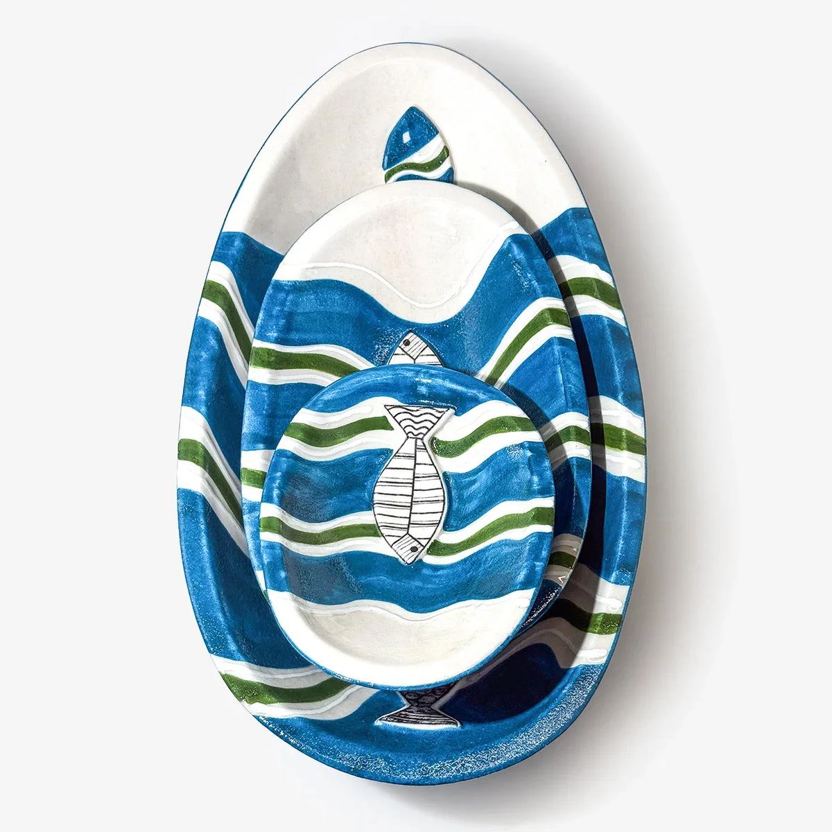 Three nested oval ceramic plates with a blue, white, and green nautical design featuring wavy stripes and fish motifs, shown on a light gray background.