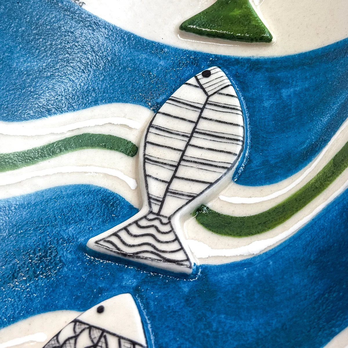 Close-up of a ceramic fish figurine with a white body, black line patterns, and a blue and white background with green accents.