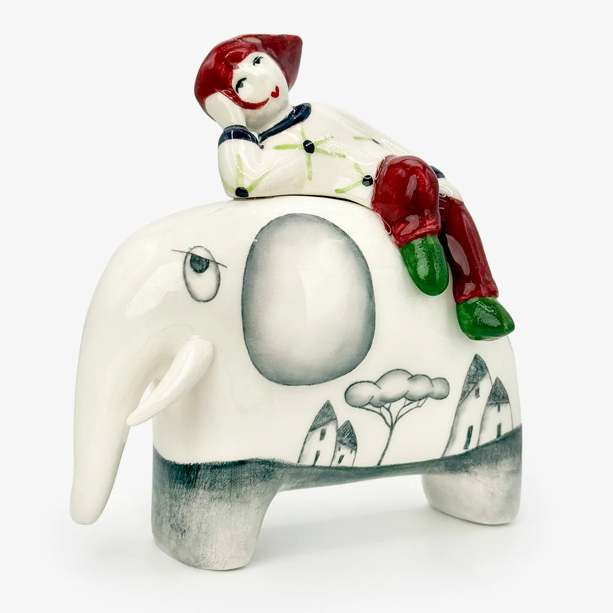 A ceramic figurine of a boy riding an elephant, set against a plain white background. The boy is dressed in red pants, green pattern sweater, red hat and boots, and green shoes.