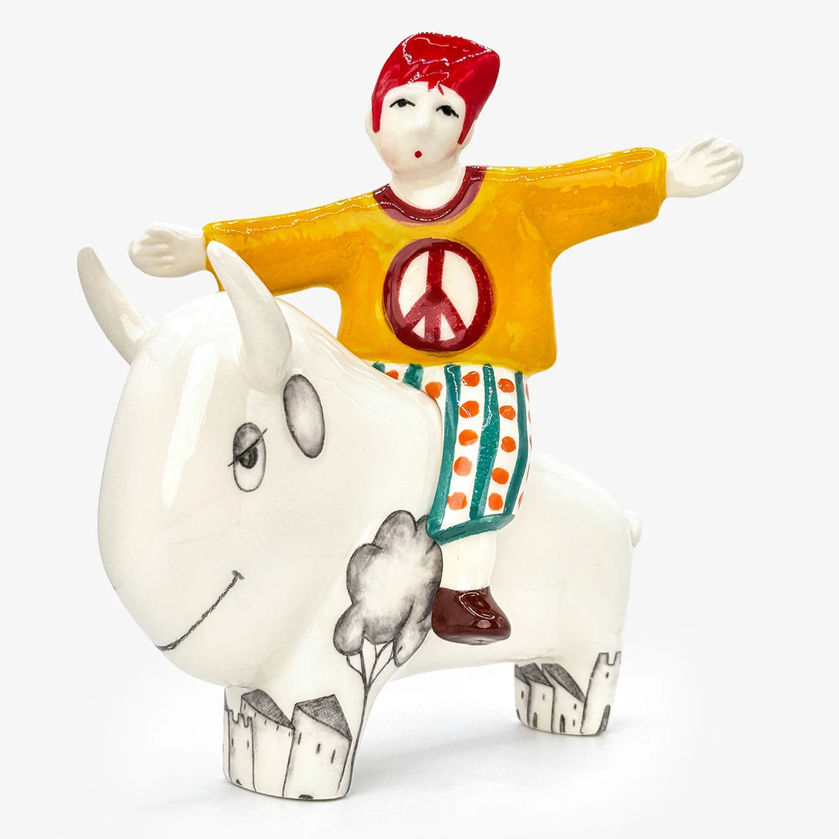 A hand-painted ceramic figurine of a child riding a white bison, set against a plain white background. The child is wearing a yellow shirt with a red peace sign, and patterned pants.