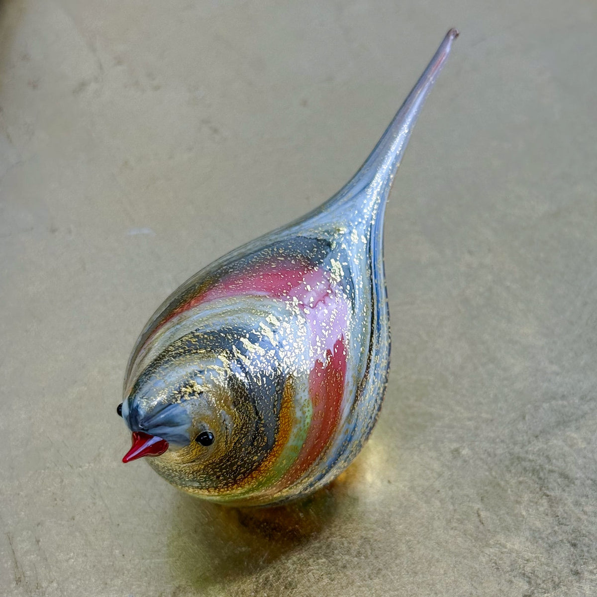 Colorful glass sculpture of a bird on a textured beige surface