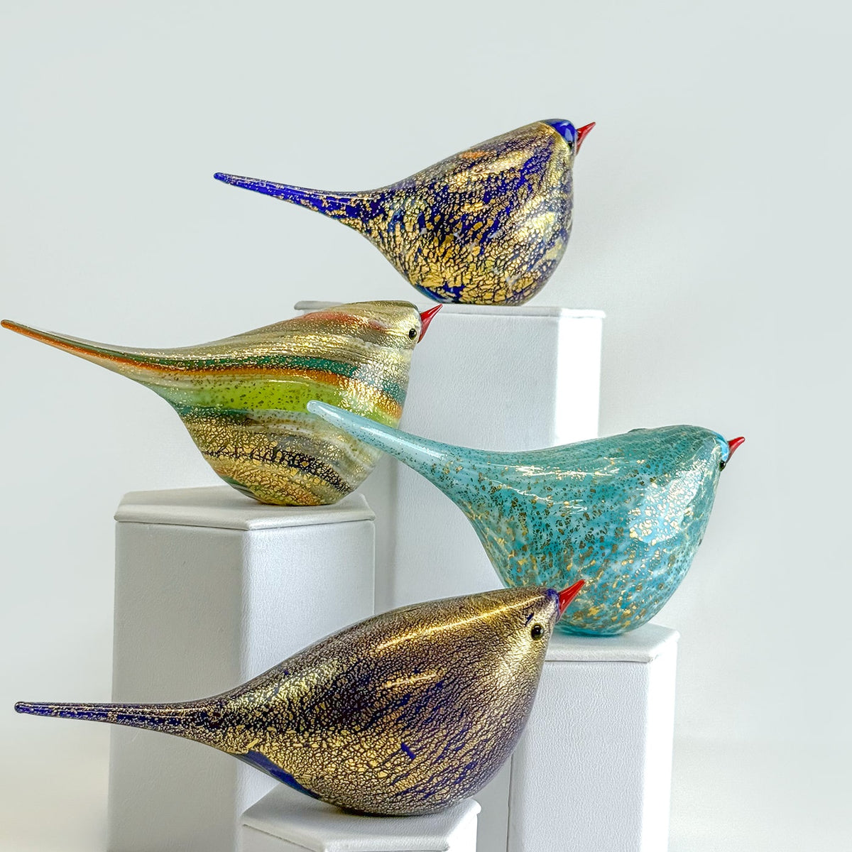 Colorful glass bird sculptures on white pedestals against a light background