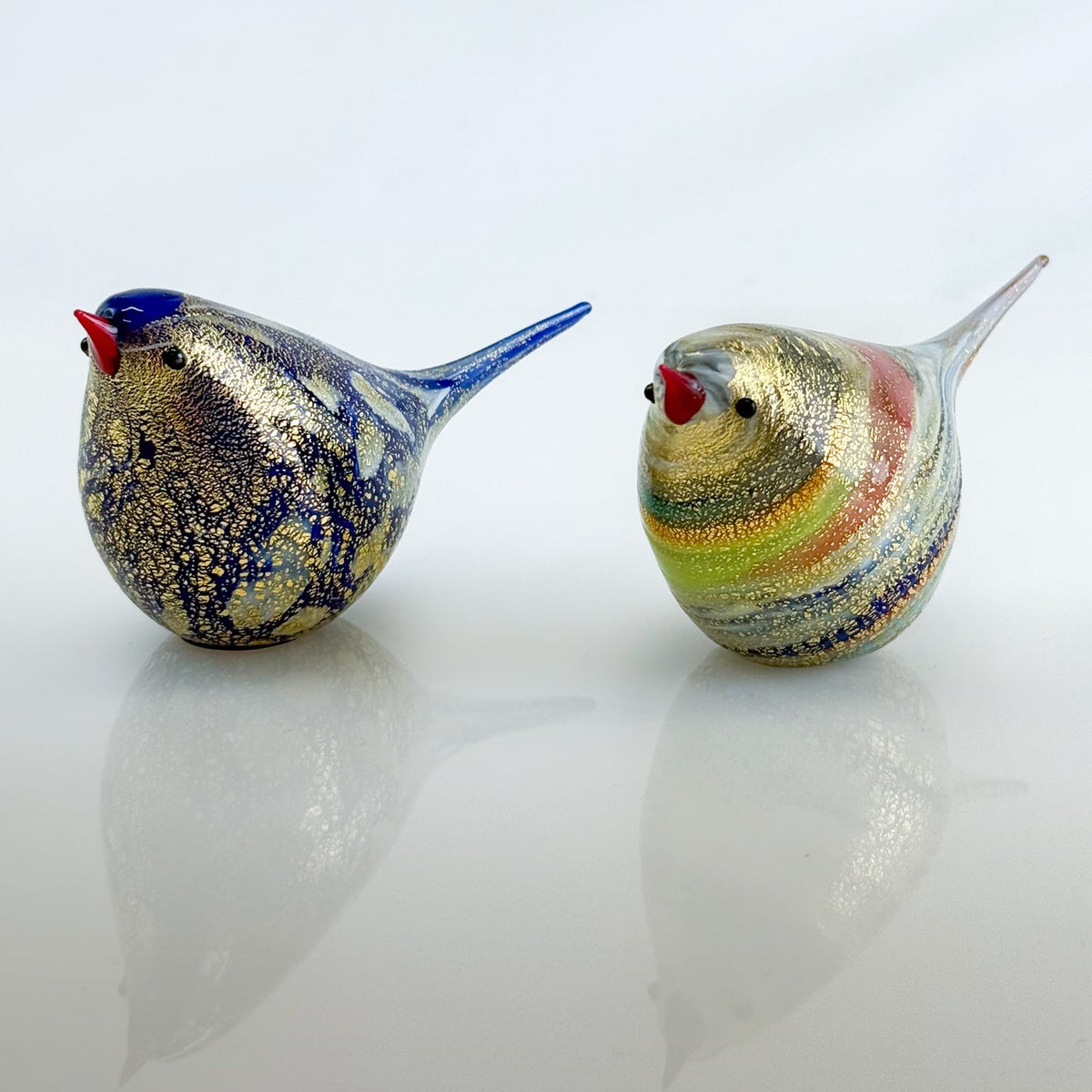 Two colorful glass birds on a reflective surface with a light gray background