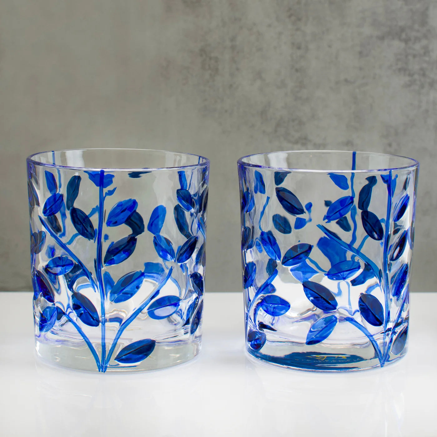 Two glass tumblers with blue leaf and vine Flowervine pattern on a gray background.