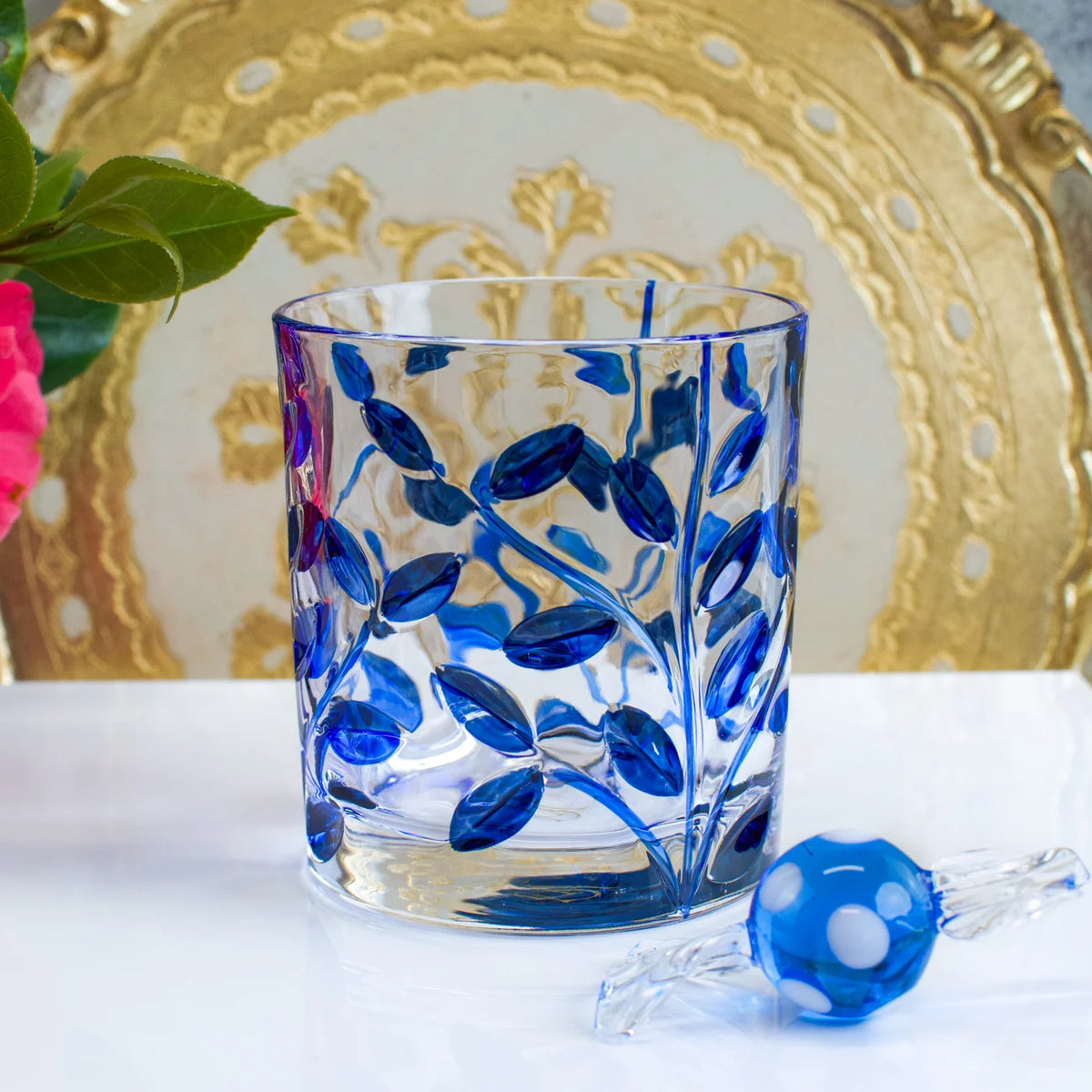 Glass tumbler with blue floral design on a white surface with a decorative gold plate in the background.