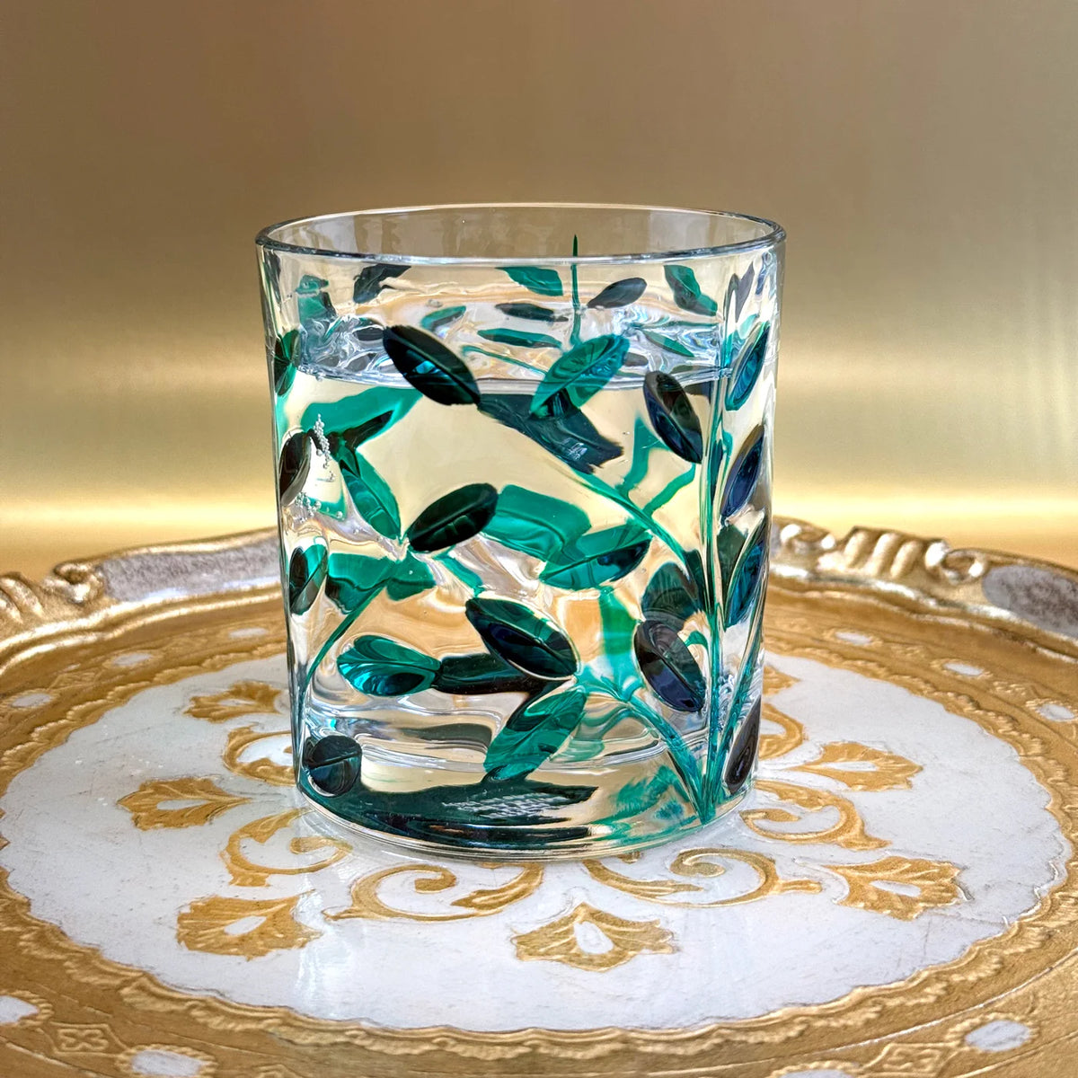Glass with green leaf pattern on a decorative carved Florentine wooden tray.