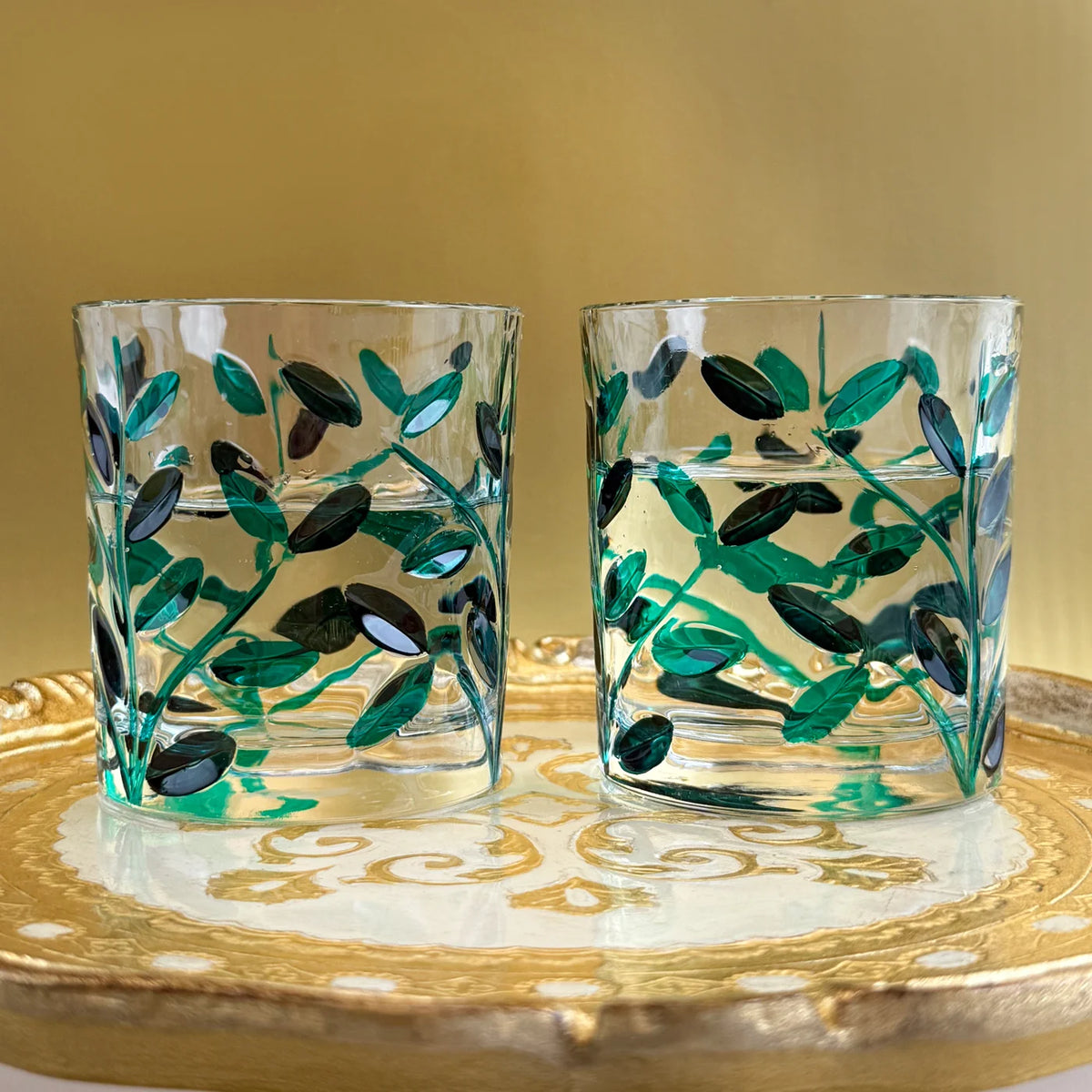 Two glass tumblers with green leaf patterns on a decorative wooden tray.