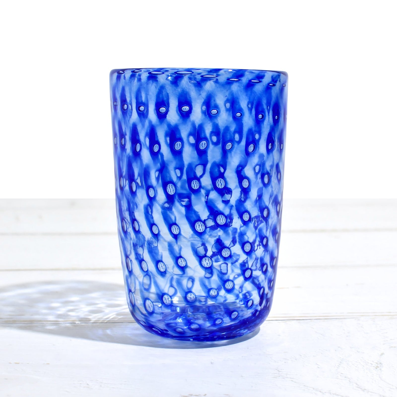 Colorful Ecco Murano tumbler glasses with orange, blue, violet, and lime hues, made in Italy, displayed on a neutral background.