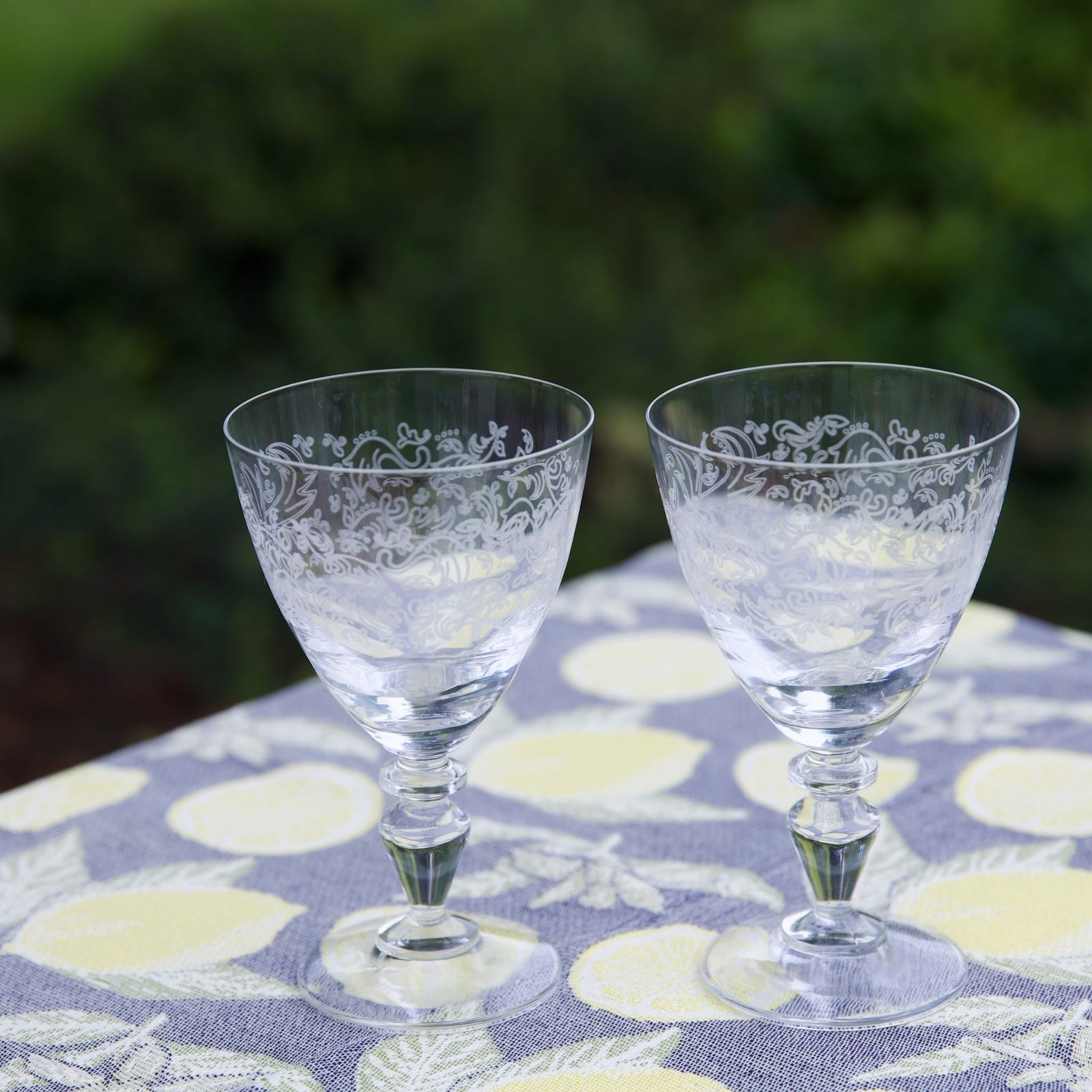 Two clear glass goblets with intricate designs on a floral-patterned tablecloth.