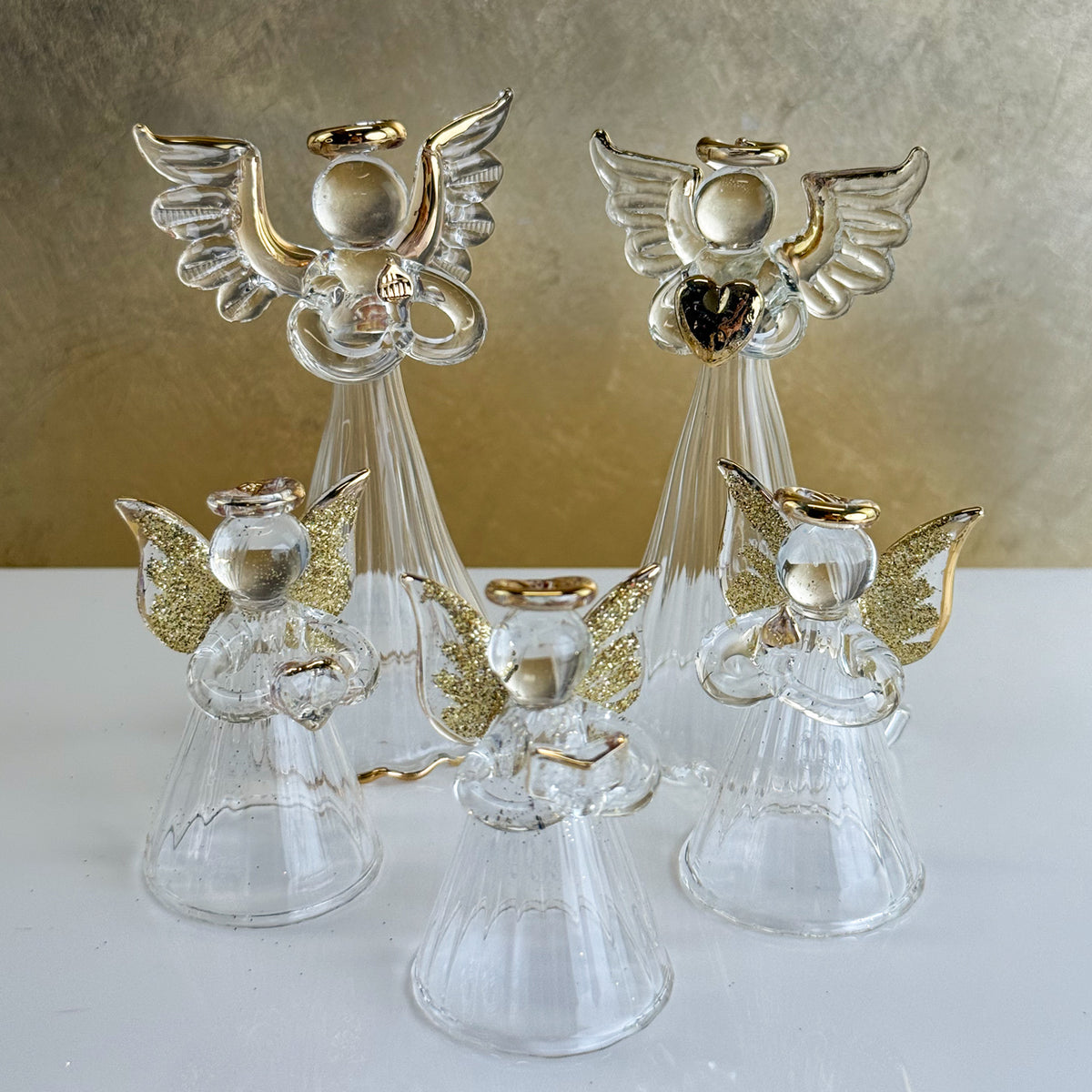 Clear angel figurines with gold accents on a white surface and beige background
