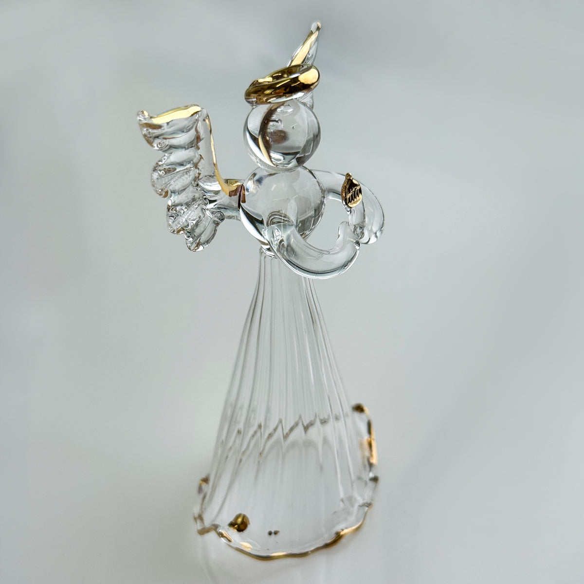 Clear glass angel figurine with gold accents on a light gray background