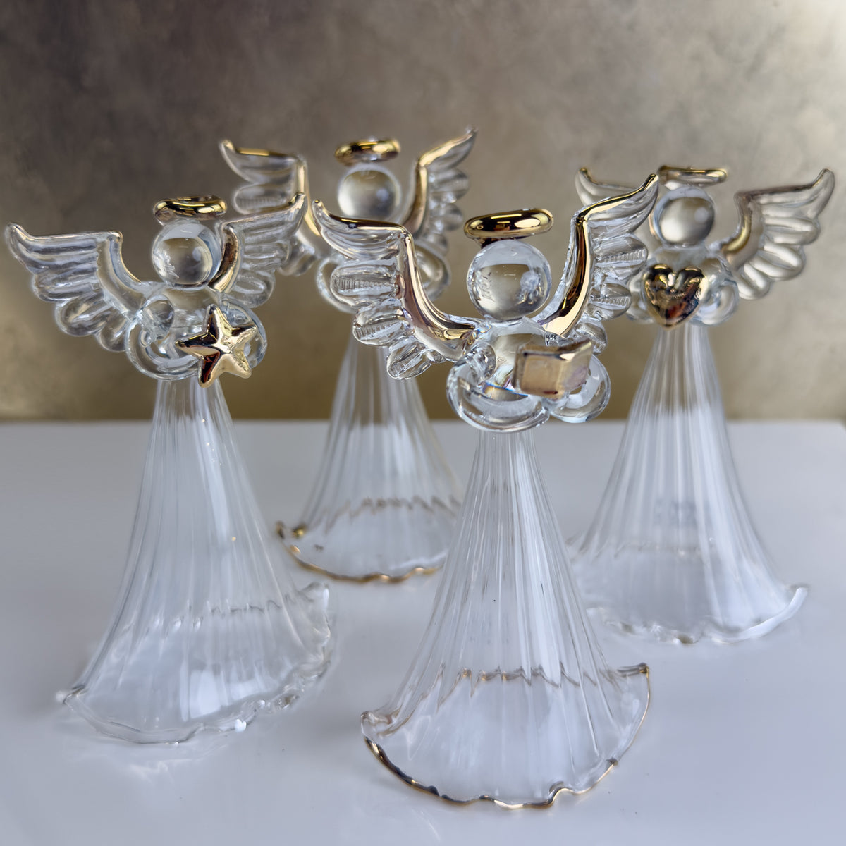 Four clear angel figurines with gold accents on a white surface.