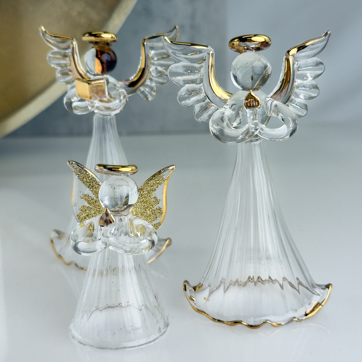 Two glass angel figurines with gold accents on a light gray background