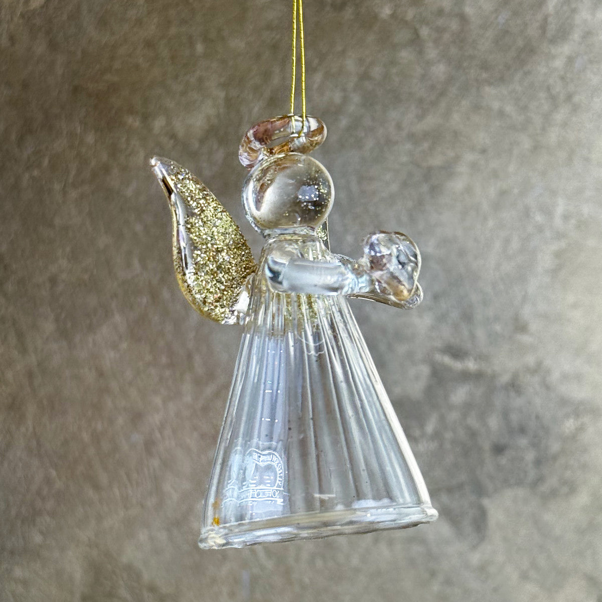 Glass angel ornament with gold glitter wings on a neutral background
