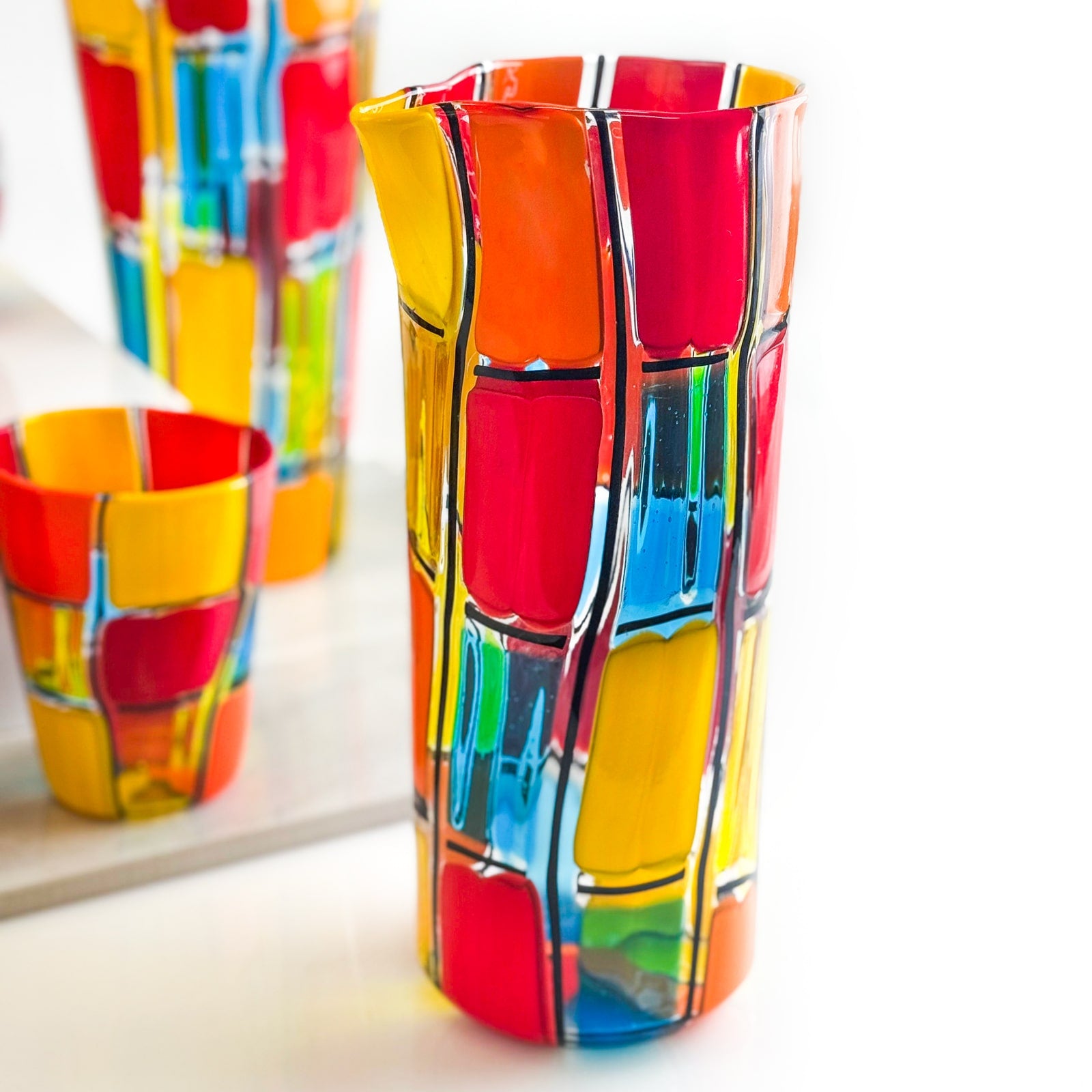 Set of two handblown Murano glass tumblers and a carafe by Pazzia, showcasing vibrant colors and elegant craftsmanship.