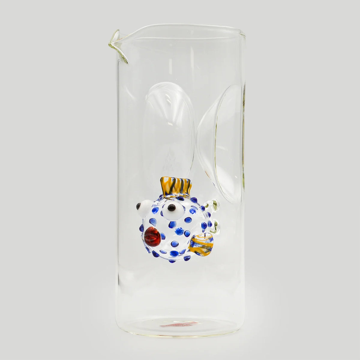 A clear glass carafe with a small hand-blown decorative puffer fish with blue spots and yellow details.