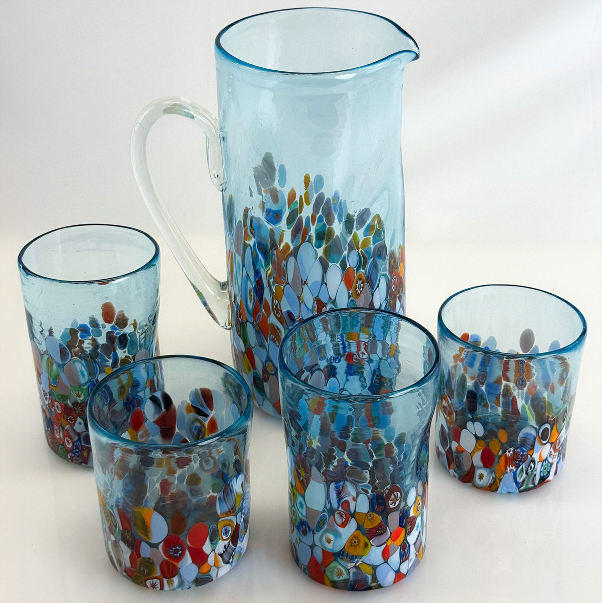 Set of colorful glass tumblers and a pitcher on a white background