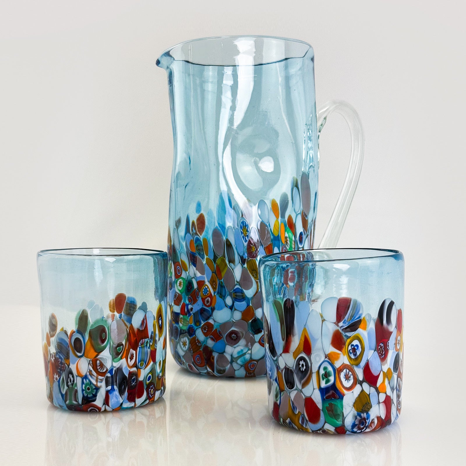 Set of colorful glass pitcher and tumblers on a light background
