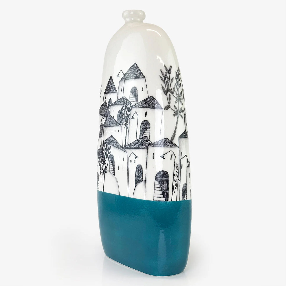 A tall, narrow ceramic vase with a glossy white upper body featuring a hand-drawn black architectural illustration of houses and trees, and a solid teal-blue lower section, set against a plain light gray background.