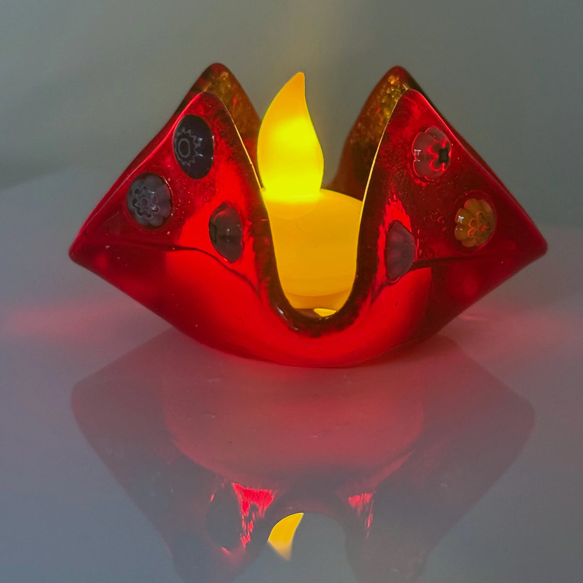 Colorful Murano glass Millefiori candle votive holder on decorative tray, made in Italy, with vibrant floral patterns.