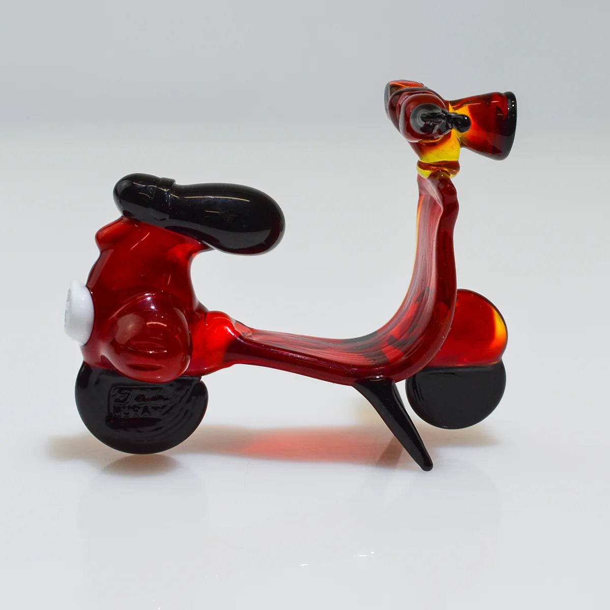 A small glass toy scooter in translucent red with black wheels, seat, and handlebar, photographed on a clean white studio background.