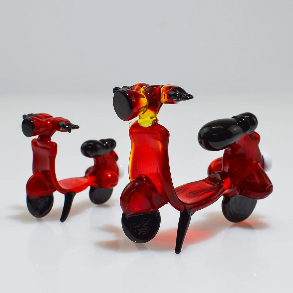 Three small translucent red glass toy scooters with black wheels, seats, and handlebars arranged on a light gray studio background.
