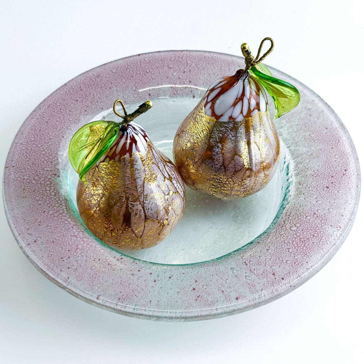 Decorative glass pears on a glass plate with a white background