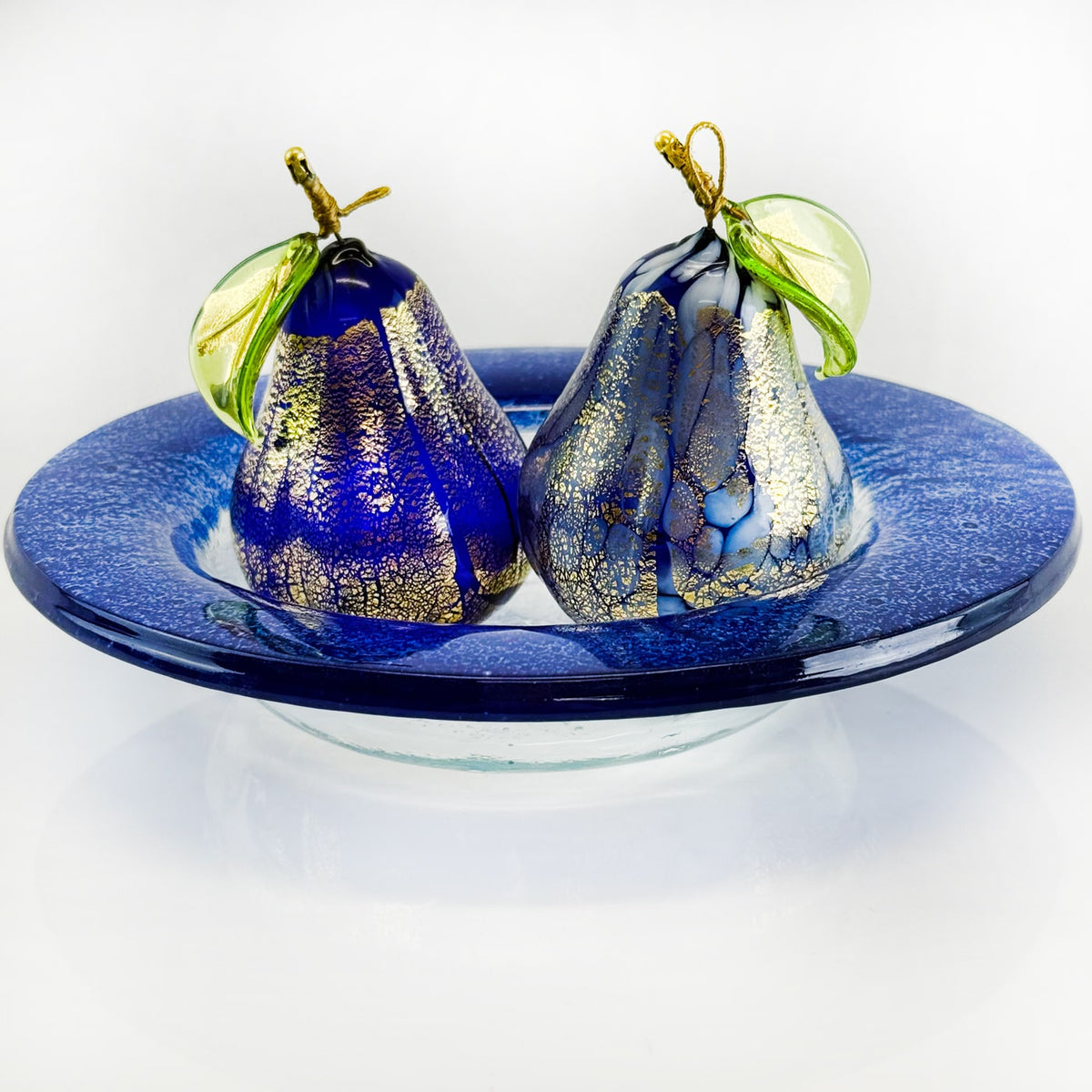 Two glass pear ornaments on a blue dish with a white background