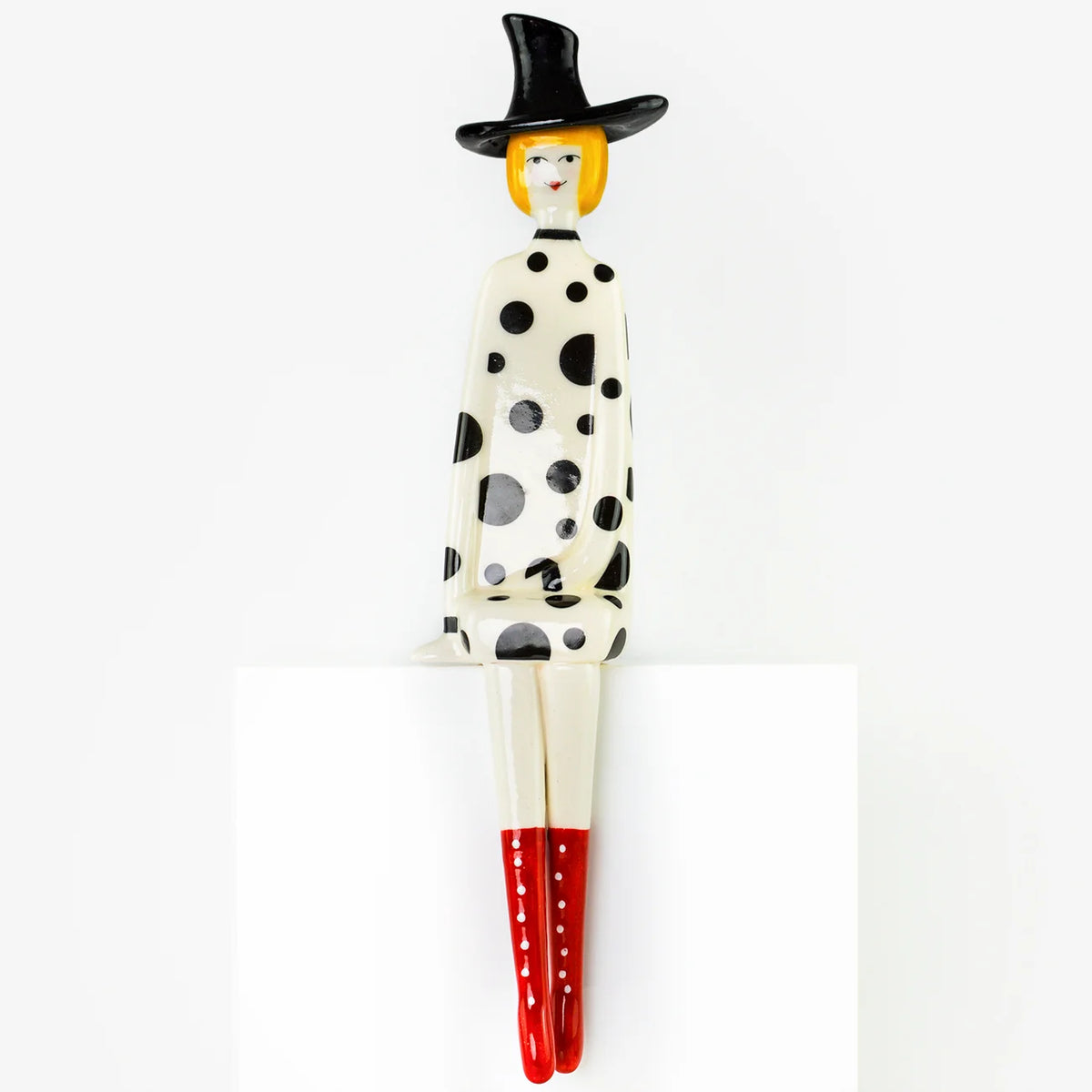 A stylized figurine of a seated woman with a black hat, black polka dots on a cream body, and red boots, displayed against a plain white background.