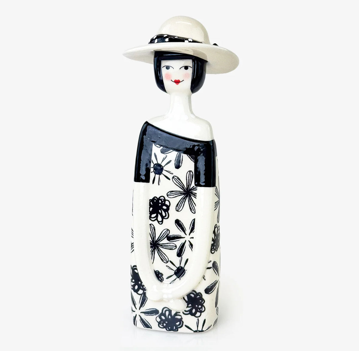 A ceramic figurine of a woman with a white hat, black hair, and a black-and-white floral dress, photographed against a clean white background.