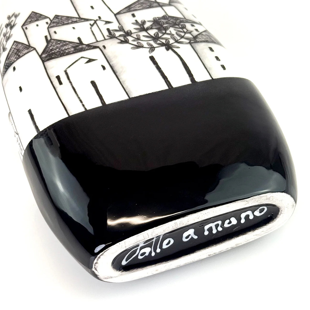 A close-up of a ceramic vase with a glossy black base and a white upper section decorated with a black hand-drawn style illustration of houses and trees.