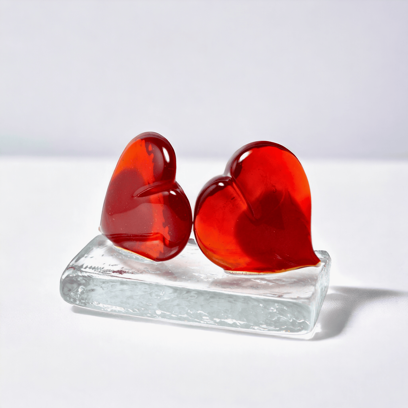 Pair of red Murano glass hearts sculpture and paperweight from MyItalianDecor, featuring vibrant red glass hearts on a cloth surface.