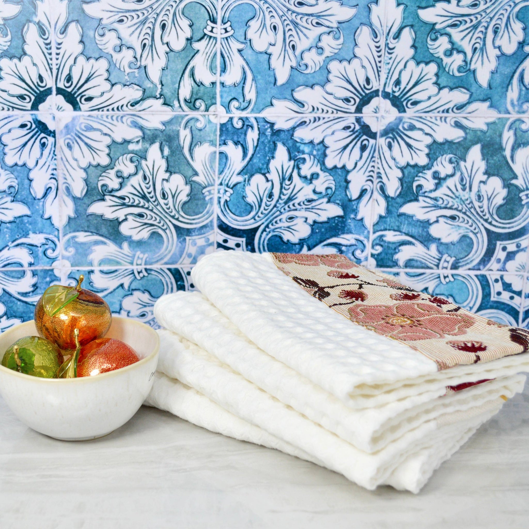 Colorful Italian kitchen towel by My Italian Decor displayed next to a bowl with Murano glass fruit, showcasing vibrant table linens.