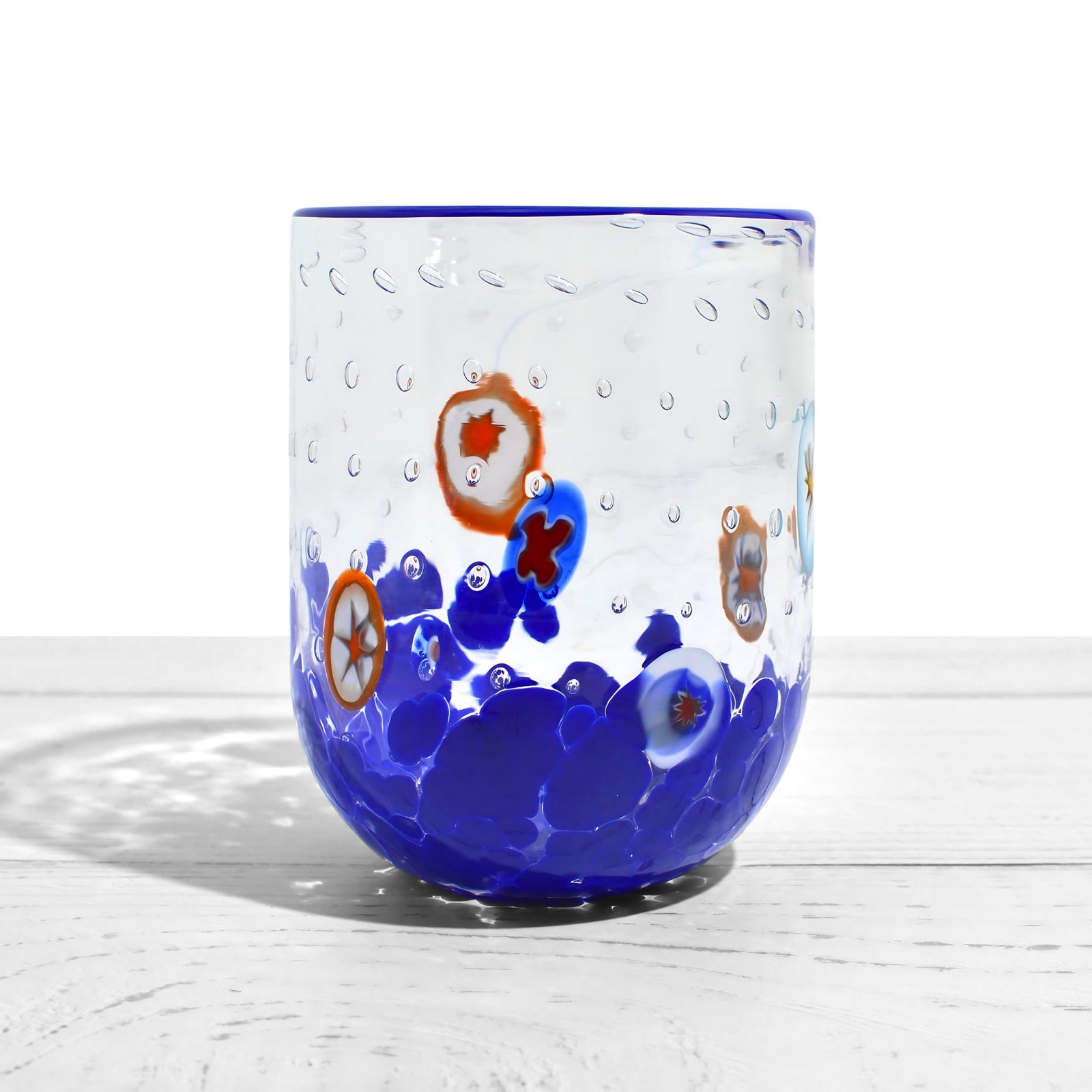 Gioia Color Millefiori Murano tumblers with vibrant glass designs, made in Italy, displayed on a wooden surface.