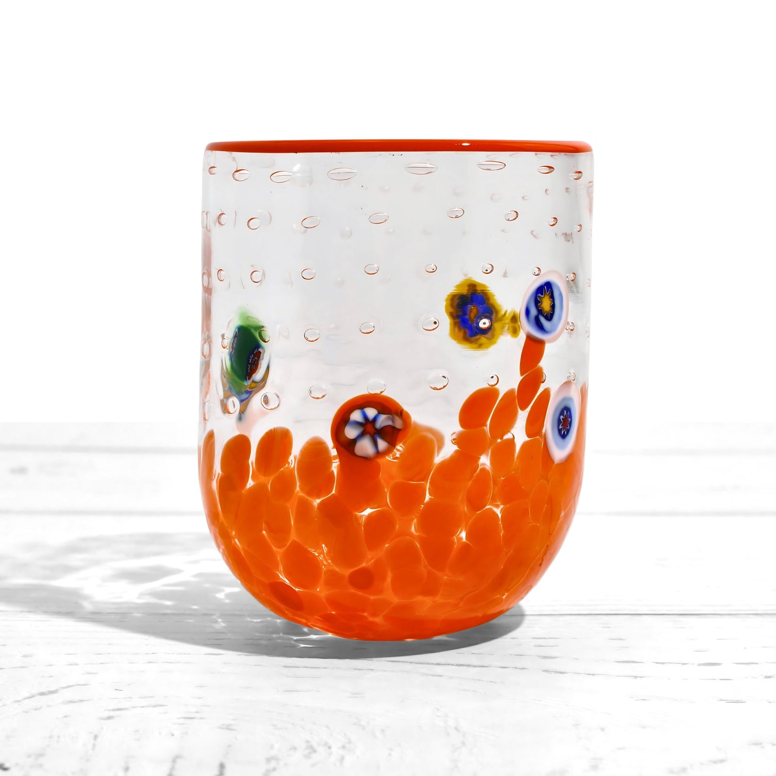 Gioia Color Millefiori Murano tumblers with vibrant glass designs, made in Italy, displayed on a wooden surface.