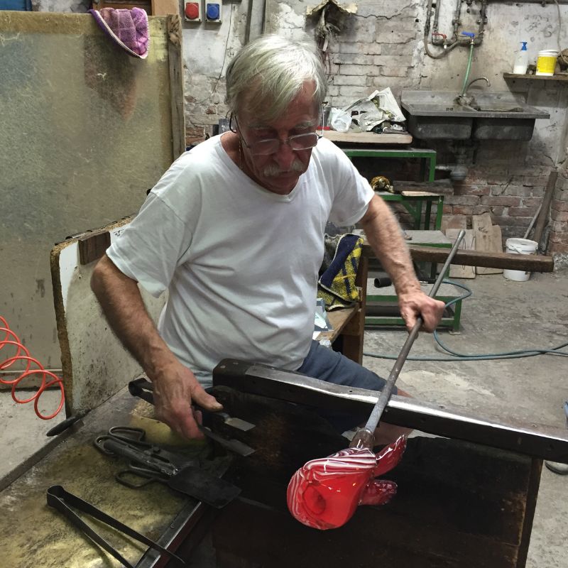Glassblower in Murano, Italy making a red vase at furnace.