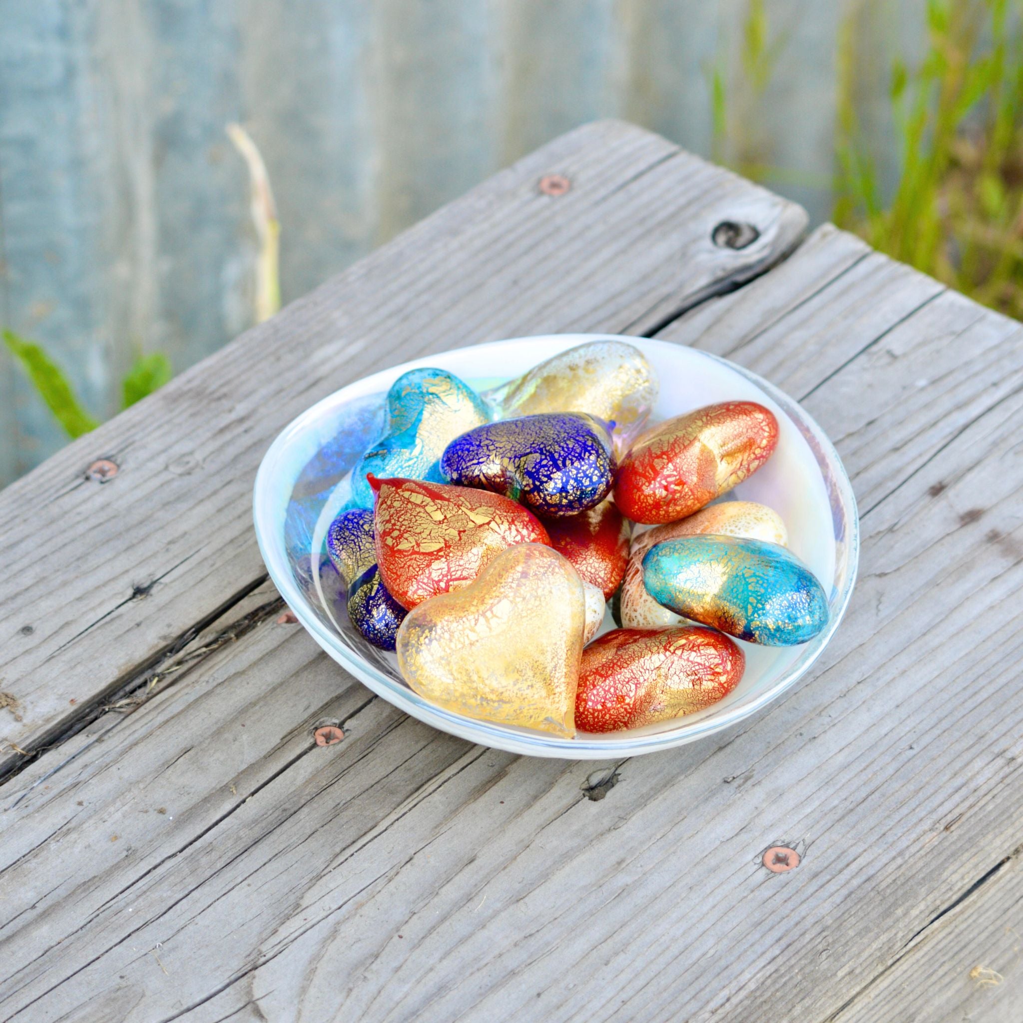 Set of three small Murano glass hearts in red, white, and blue, Italian-made figurines displayed in a bowl.