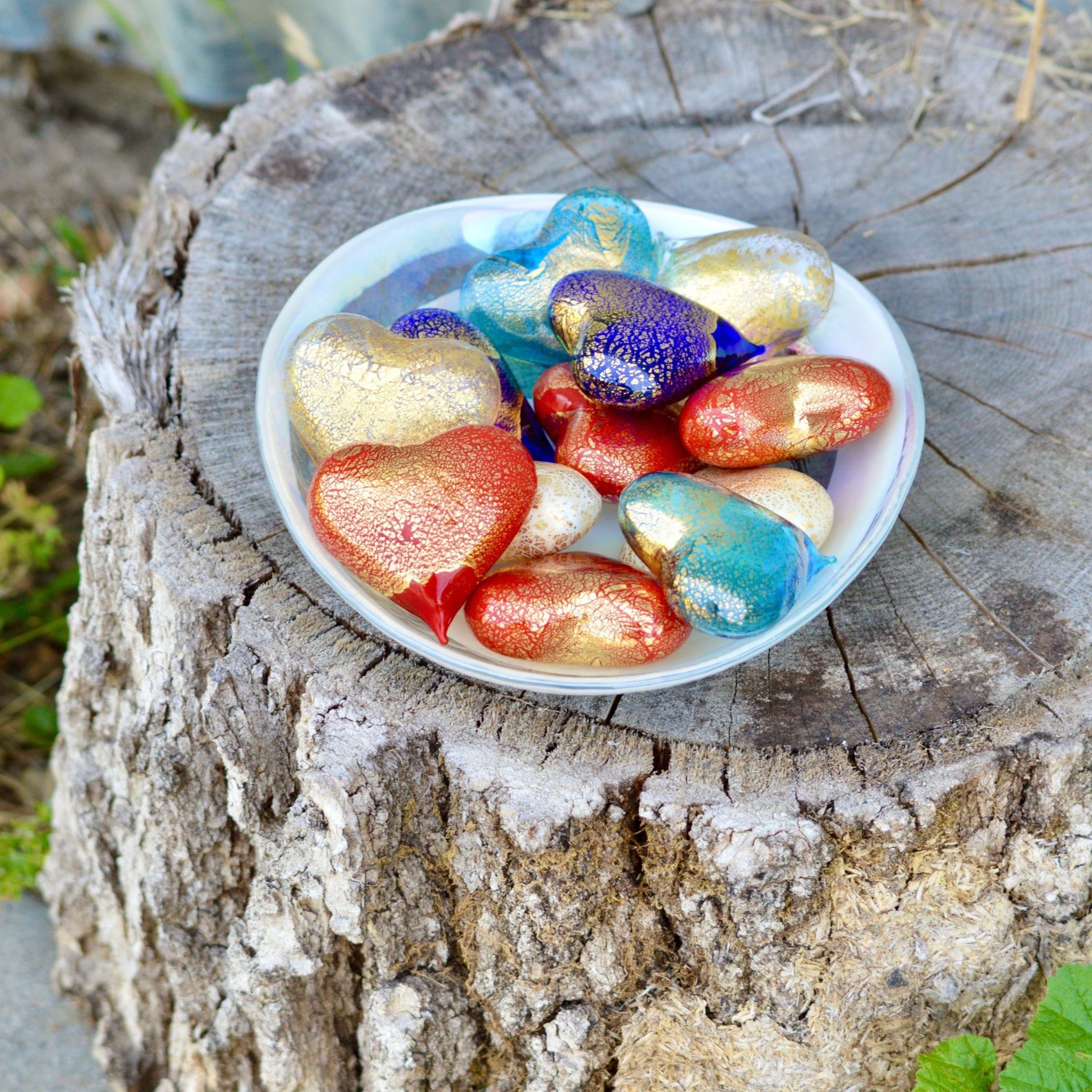 Set of three small Murano glass heart figurines in red, white, and blue, made in Italy, displayed in a bowl.
